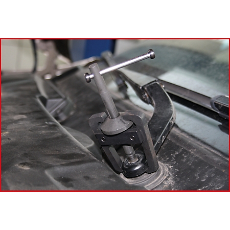 Detailaufnahme eines schwarzen Werkzeugs, das auf einem schmutzigen Autoteil montiert ist, vermutlich um einen Scheibenwischer zu entfernen.